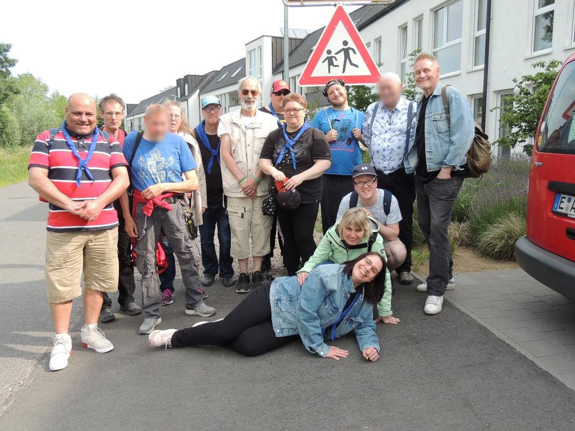 Gruppenbild der Fahrt 2018 nach Bocholt-Suderwick: 14 Personen mit blauem Halstuch, im Hintergrund eine Wohnsiedlung