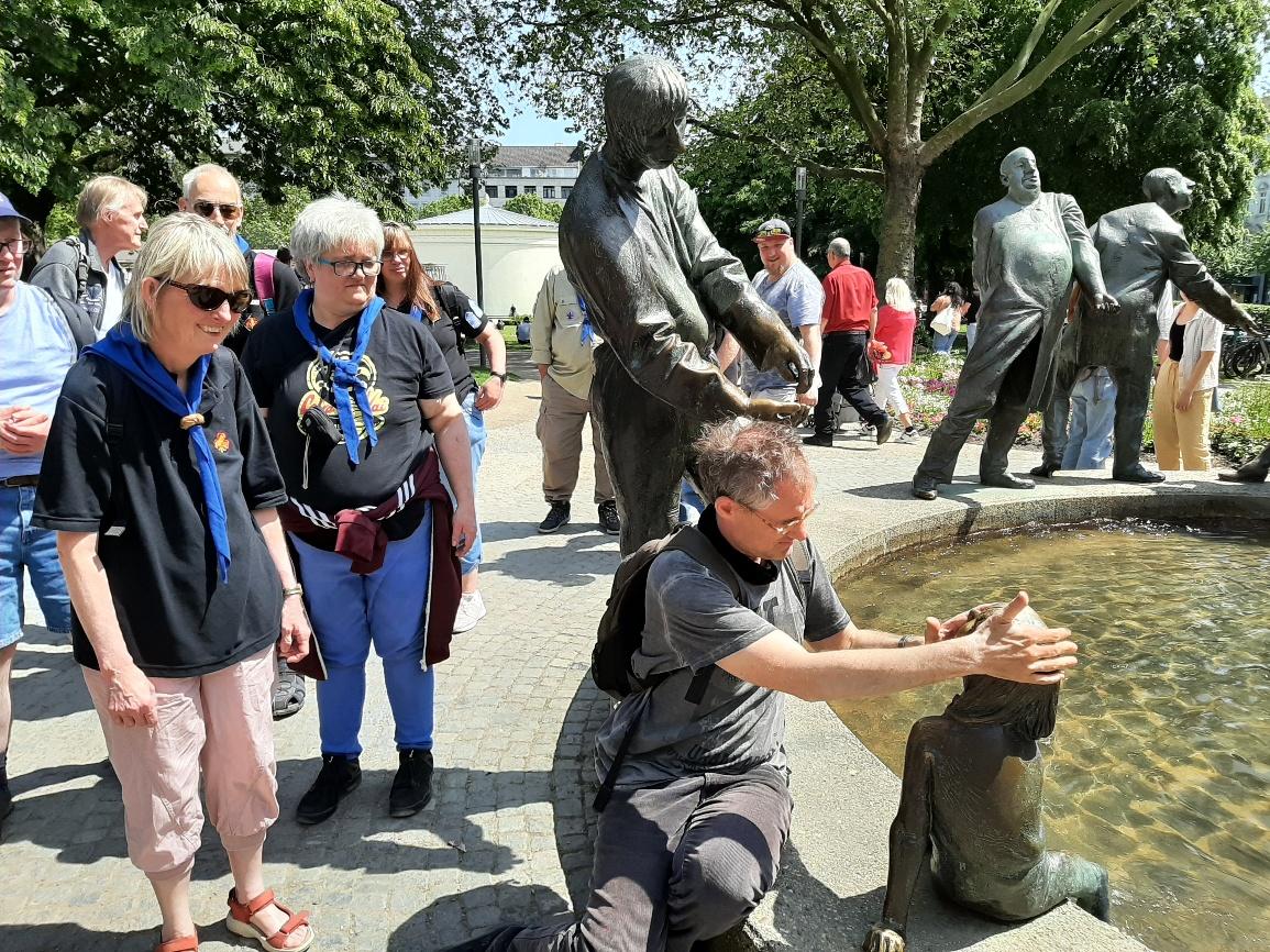 Gruppenbild der Fahrt 2023 nach Aachen: neun Personen am Brunnen „Kreislauf des Geldes“
